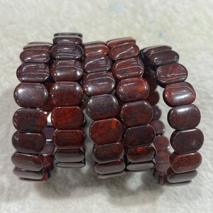 May include: Five red jasper bracelets stacked on top of each other. Each bracelet is made of oval-shaped beads.