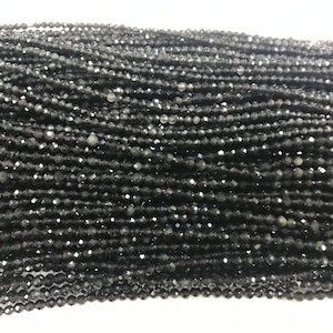 Puede incluir: Una hebra de cuentas de piedras preciosas facetadas negras. Las cuentas son pequeñas y redondas, y tienen una superficie brillante y reflectante.