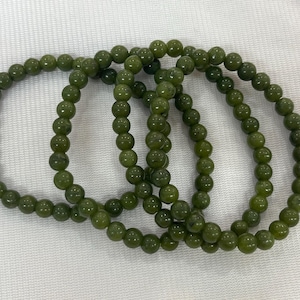 Könnte beinhalten: Drei kreisförmige Armbänder, die aus glatten, runden, olivgrünen Perlen bestehen. Jedes Armband weist eine gleichmäßige Anordnung polierter, kugelförmiger Perlen auf, die zu einer durchgehenden Schlaufe aufgereiht sind und eine einheitliche dunkelgrüne Farbe zeigen.