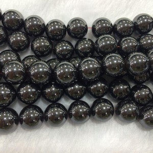 May include: A strand of black hematite beads, each bead is round and smooth. The beads are strung on a thin red thread.