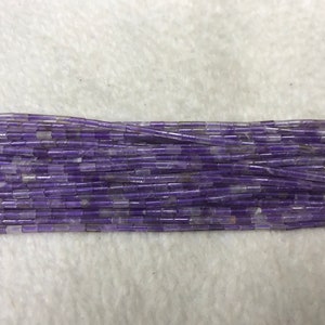 Peut inclure: Un brin de perles d'améthyste violettes, chaque perle est de forme rectangulaire avec un bord légèrement arrondi.