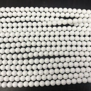 May include: A strand of white round beads, likely made of ceramic or porcelain. The beads are smooth and uniform in size and shape.