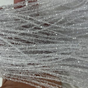 May include: Close-up of multiple strands of clear, faceted beads. The beads are strung together, creating a shimmering, textured effect. The beads are small and appear to be made of a transparent material, reflecting light.