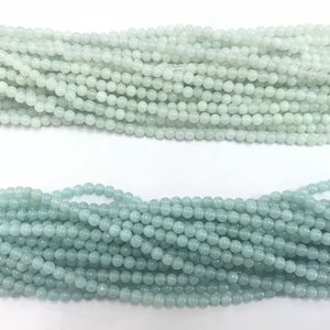 Puede incluir: Una hebra de cuentas redondas de color azul claro hechas de jade. Las cuentas son de tamaño uniforme y tienen un acabado liso y pulido.