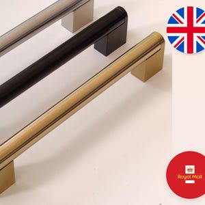 May include: Three cabinet door pulls in different finishes: brushed nickel, black, and gold. The pulls are all the same size and shape, with a rounded rectangular design.