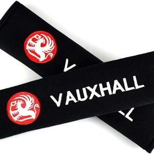 May include: Two black seatbelt covers with white embroidered text "VAUXHALL" and a red embroidered logo of a white griffin.
