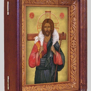 May include: A religious icon depicting Jesus Christ as the Good Shepherd, carrying a lamb on his shoulders. He is wearing a red robe and a blue tunic, and holding a shepherd's staff. The icon is framed in a wooden frame with intricate carvings.