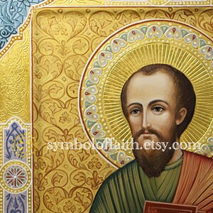 May include: A hand-painted icon of a saint holding a book. The icon is set against a gold background with intricate floral designs. The saint is depicted with a halo and a beard. The icon is framed in a gold frame with a blue and white border.