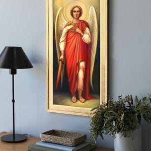 Pode incluir: Uma pintura emoldurada do Arcanjo Miguel, um &iacute;cone religioso com uma aur&eacute;ola dourada, segurando uma espada e vestindo uma t&uacute;nica vermelha e uma armadura branca. A pintura est&aacute; em uma prateleira de madeira com livros e uma cesta de vime.