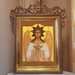 May include: A framed icon depicting an angel with wings, wearing a white robe and a gold crown. The angel has a halo with a star and the letters "IC XC" in the background. The frame is ornate and has a gold finish.
