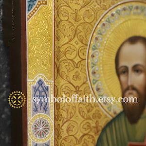 May include: A hand-painted icon of a saint with a gold background and intricate floral details. The icon is framed in a wooden frame with a gold border and a blue and white floral design.