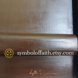 May include: A dark brown wooden frame with a gold star and the text "symboloffaith.etsy.com". The frame is signed "Lylia Tatiana 202".