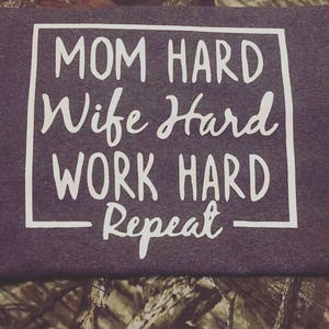 May include: A dark purple t-shirt with white text that reads "MOM HARD Wife Hard WORK HARD Repeat".