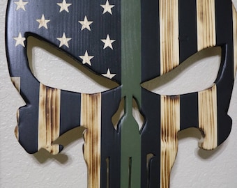 May include: Wooden skull cutout with an American flag design. The flag is painted in black, white, and brown with a green stripe down the centre.