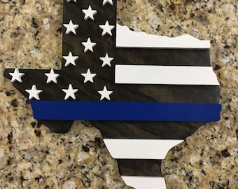 May include: Wooden cutout of the state of Texas in the shape of the American flag with a blue line across the middle. The flag is painted in red, white, and blue.