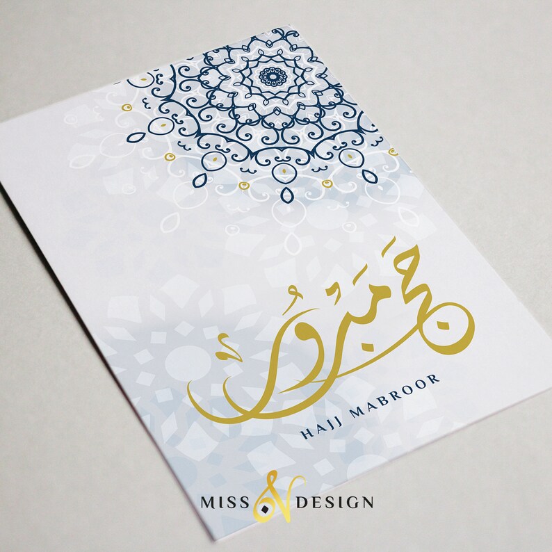 May include: A white card with a blue and gold mandala design. The card has the Arabic word for "Hajj Mabroor" written in gold calligraphy. The card also has the text "Miss V Design" in the bottom left corner.