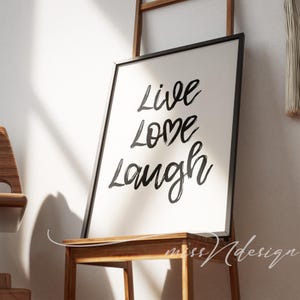 May include: A framed art print with the words "Live Love Laugh" in black script on a white background. The frame is black, and the print is displayed on a wooden chair.