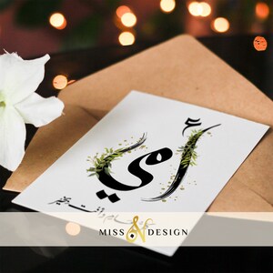 May include: A white card with black calligraphy that says "Mom" in Arabic script. The calligraphy is decorated with green leaves and gold glitter. The card has the text "Miss & Design" in gold lettering at the bottom.