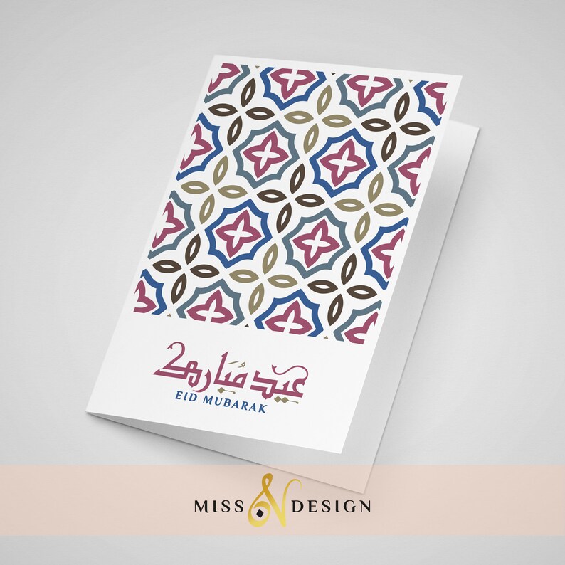 May include: A white card with a geometric pattern in shades of blue, brown, and pink. The card has the text "Eid Mubarak" in Arabic script and the English translation below. The card is folded in half and has a white background.