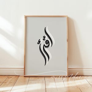 Peut inclure: Une impression d'art mural verticale encadrée présentant un fond gris clair avec un motif central de calligraphie arabe en noir et blanc. L'œuvre est insérée dans un cadre en bois clair fin, offrant une composition équilibrée et épurée.