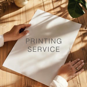 Peut inclure: Une feuille de papier rectangulaire blanche avec le texte gris foncé PRINTING SERVICE centré sur la page. Le papier est posé sur une surface en bois avec une lumière naturelle projetant des ombres sur la surface et le papier lui-même.