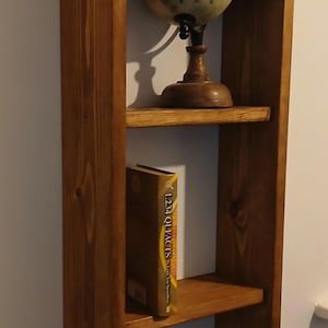 May include: A wooden bookshelf with three shelves. The top shelf holds a globe on a wooden stand. The middle shelf has a book with the title "1234 QI FACTS". The bottom shelf holds a CD case and a remote control.