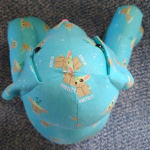 May include: A light blue plush toy with a repeating pattern of a cartoon character and stars. The toy has black button eyes and the words "ATTACK" and "PROTECT" printed on it.