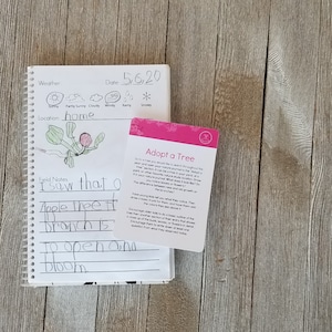 May include: A spiral-bound notebook with handwritten notes and a drawing of a tree, next to a pink card that says "Adopt a Tree". The notebook has weather icons and the date 5/6/20.