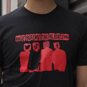 May include: Black t-shirt with the text "RAGE AGAINST THE ALGORITHM" in red, featuring red silhouettes of people with social media icons: Twitter, TikTok, Instagram, and Facebook.