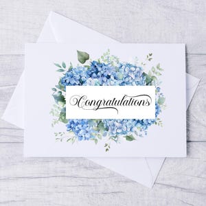 May include: A white greeting card featuring a floral design of blue hydrangeas and green foliage. The card displays the word "Congratulations" in cursive script. The card rests on a white envelope.