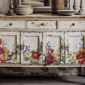 Pu&ograve; includere: Un mobile in legno bianco invecchiato con decalcomanie floreali. Il mobile ha due cassetti e due ante con motivi floreali in tonalit&agrave; di rosso, giallo e blu.