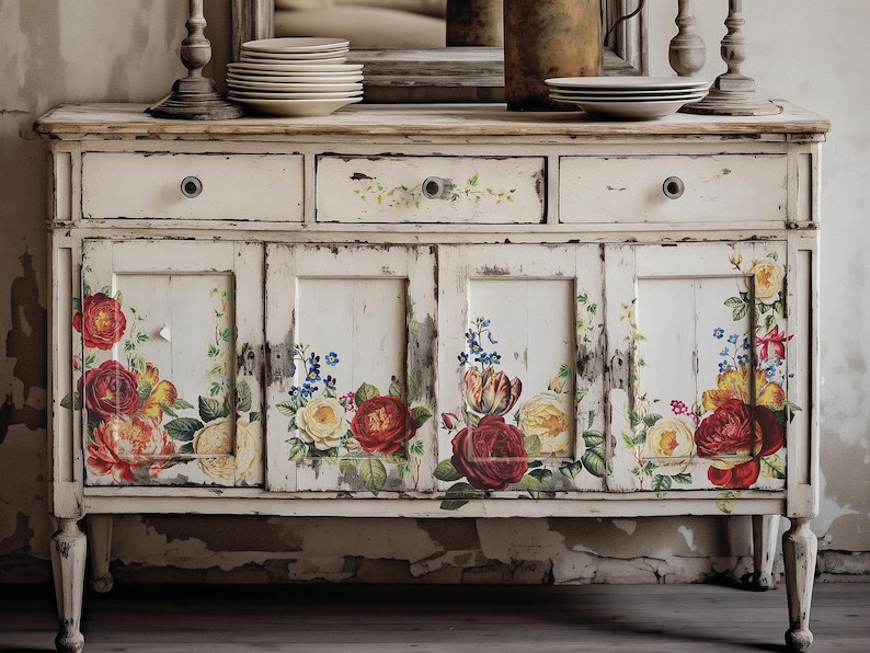 Pu&ograve; includere: Un mobile in legno bianco invecchiato con decalcomanie floreali. Il mobile ha due cassetti e due ante con motivi floreali in tonalit&agrave; di rosso, giallo e blu.