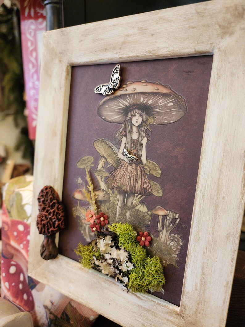Pu&ograve; includere: Un'illustrazione incorniciata di una ragazza in un bosco di funghi. La ragazza indossa un vestito rosa e tiene una farfalla. La cornice &egrave; decorata con muschio, fiori e un fungo.