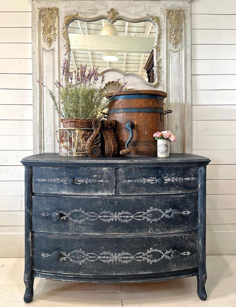 Pu&ograve; includere: Un antico com&ograve; dipinto di nero con tre cassetti e un fronte curvo. I cassetti presentano un motivo a stencil decorativo in vernice bianca. Il com&ograve; &egrave; appoggiato su un pavimento di legno.