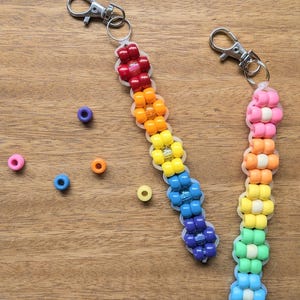 Könnte beinhalten: Zwei Schlüsselanhänger mit Perlen in Regenbogenfarben. Einer hat rote, orange, gelbe, grüne, blaue und violette Perlen. Der andere hat rosa, orange, gelbe, grüne und blaue Perlen. Beide haben silberne Verschlüsse.