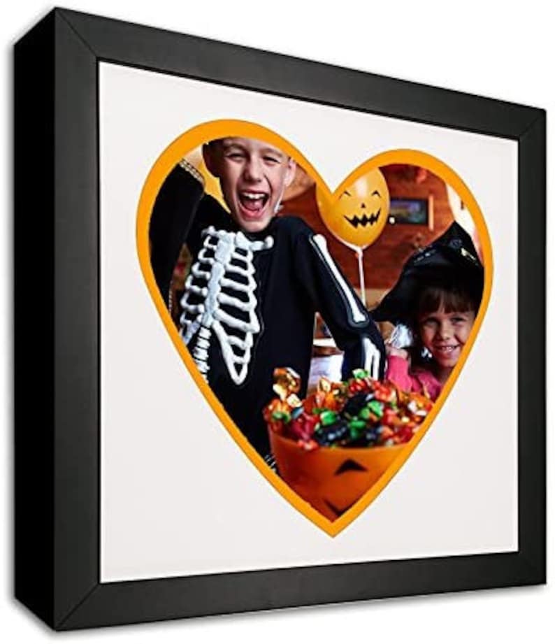 May include: Two children dressed in Halloween costumes, one in a skeleton costume and the other in a witch costume, are holding a bucket of candy. The image is in a heart shape with an orange border.