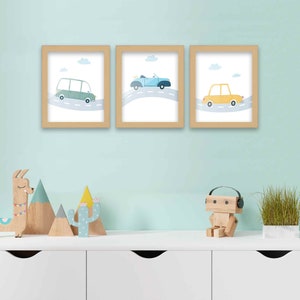 May include: Three framed prints with a light blue background and white clouds. Each print features a different cartoon car driving on a winding road. The cars are blue, green, and yellow.