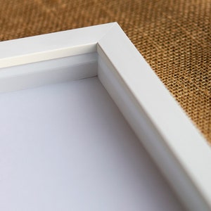 May include: Close-up of the corner of a white picture frame. The frame has a simple, clean design and is made of a smooth, white material.