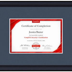 May include: A framed CompTIA Security+ Certificate of Completion for Jessica Baxter, dated October 15, 2022. The document features red corner accents, black text, and two signatures, all encased in a black frame with a dark blue matting border.