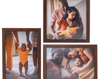 May include: Three rectangular picture frames with a dark brown wood grain finish. The frames contain photographs of a family, including a baby in a yellow outfit, a parent holding the baby, and a family lying together on a bed with soft lighting.