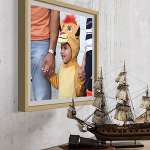 May include: A framed photograph of a child dressed as a lion, holding hands with two adults. The child is smiling and looking at the camera. The photo is in a light brown frame.