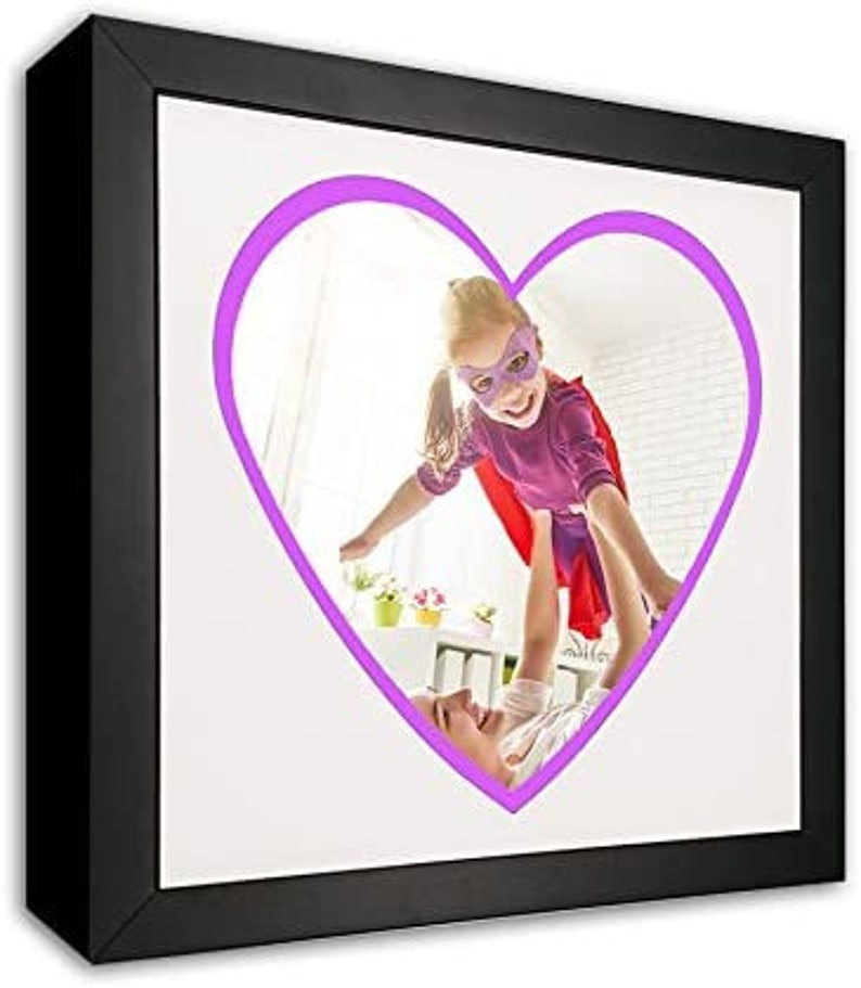 May include: A black picture frame with a white mat and a purple heart-shaped outline around a photo of a child wearing a purple superhero costume and a mask, flying through the air while being held by an adult.