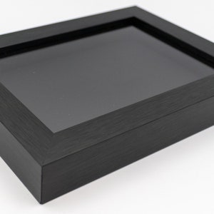 May include: A black wood picture frame with a clear glass insert. The frame is made of a wood with a wood grain pattern.