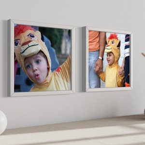 May include: Two square white frames mounted on a wall, each displaying a photograph of a child wearing a yellow lion costume with a bright red mane. The frames are positioned above a surface featuring a round white vase and a stacked ceramic vase.