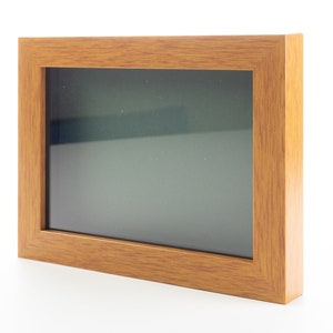 May include: A rectangular wooden picture frame with a light brown finish. The frame has a dark gray interior and is set against a white background. The frame is designed to hold a photograph or artwork.