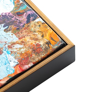 May include: Close-up of a framed abstract painting with a black frame and a gold wood-like border. The painting features a swirling mix of blue, orange, red, and white colors.