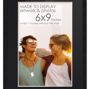 May include: Black picture frame with a white mat. The frame is made to display artwork or photos that are 6x9 inches or 8x11 inches without the mat. The image inside the frame shows a couple smiling at each other.