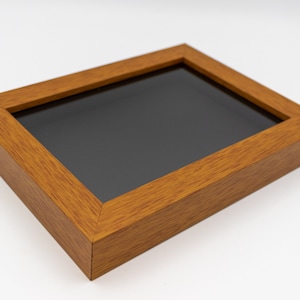 May include: A wooden picture frame with a dark gray mat. The frame is a light brown color and has a wood grain texture.