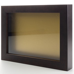 May include: A dark brown wood picture frame with a clear glass front and a gold-toned mat.