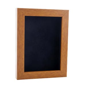 May include: A wooden picture frame with a black mat. The frame is a light brown color and has a simple design.